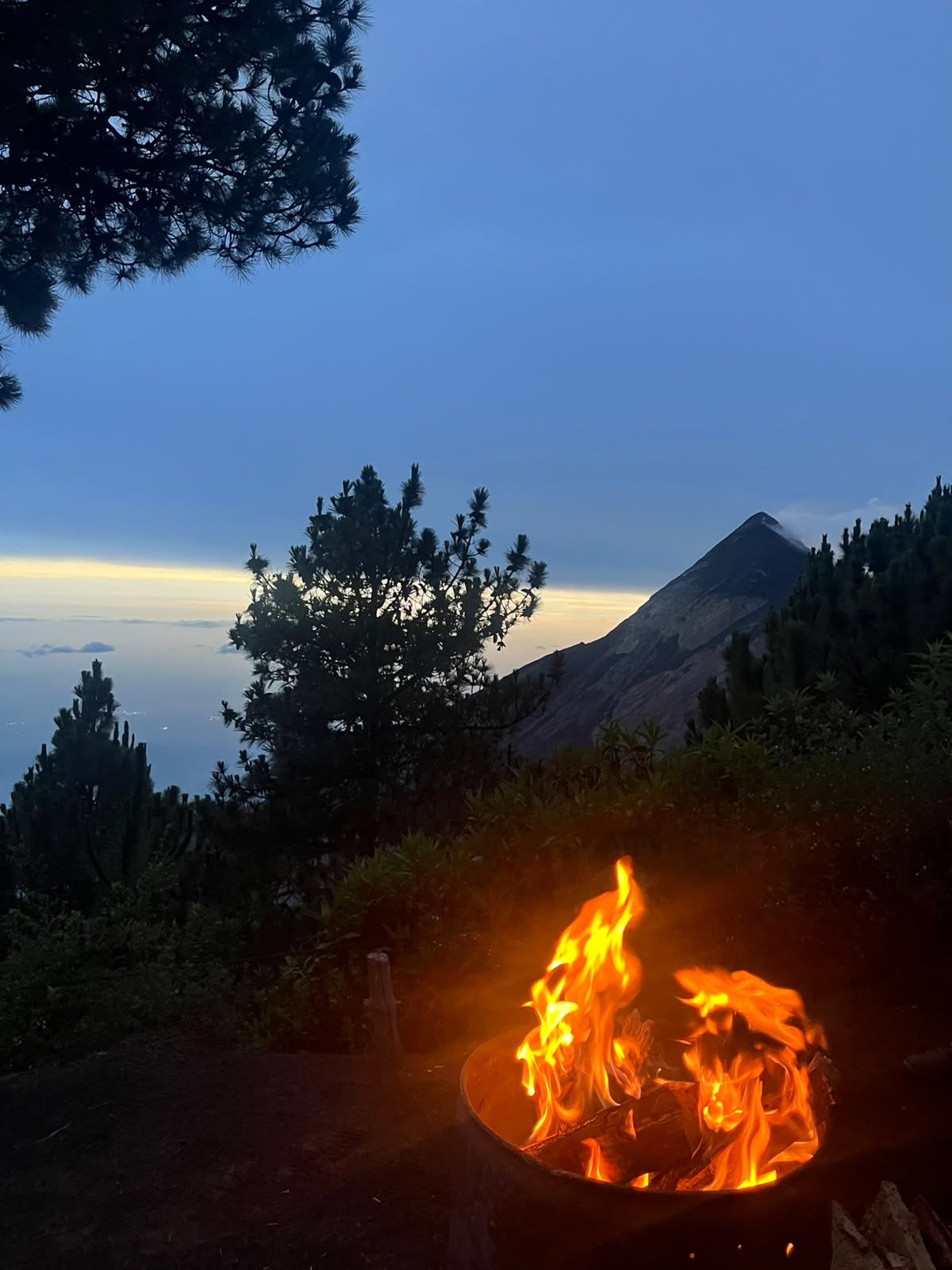 Campfire burning at Acatenango base camp with Fuego volcano in the background