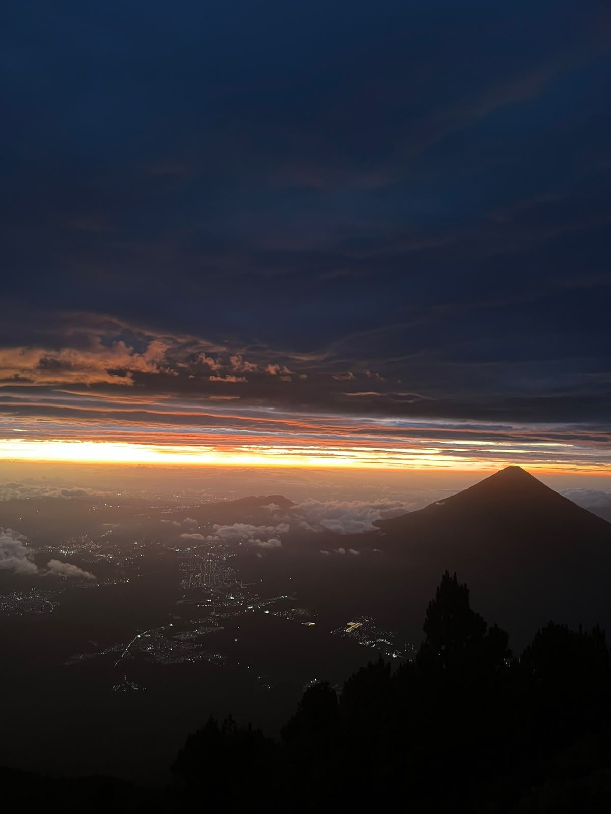 Orange sunrise over Agua volcano with the valley city lights still glowing below Acatenango camp