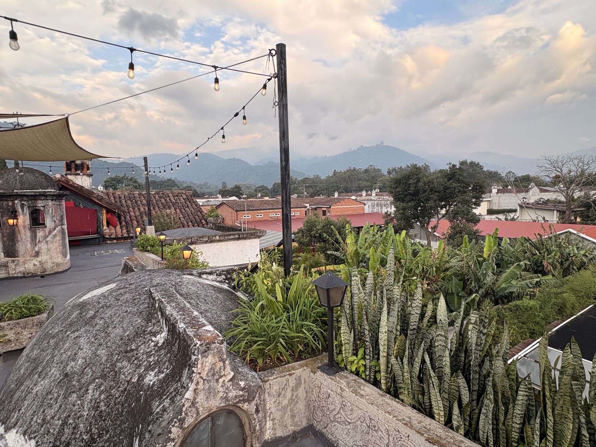 Rooftop garden in Antigua Guatemala with string lights, a church tower and mountains at dusk