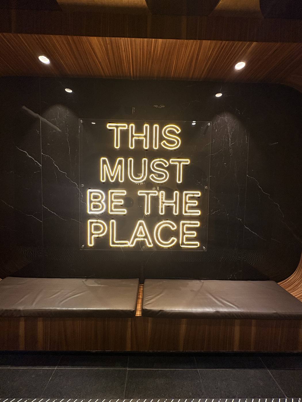 Neon sign reading This Must Be The Place inside a dark wood-and-marble interior in Guatemala City