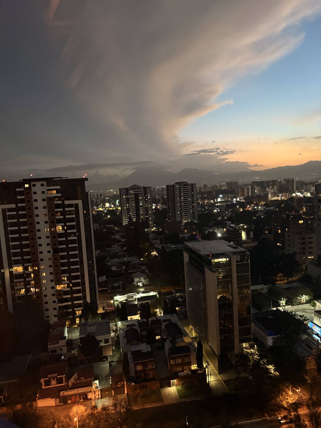 Guatemala City skyline at dusk with a mountain ridgeline behind the towers